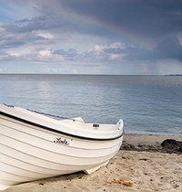 Foto eines weißen Ruderbootes am Meer mit wolkigem Himmel